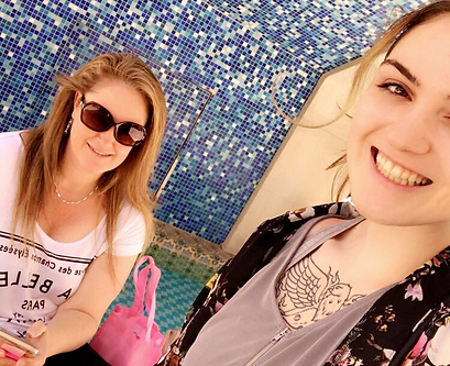 Two women smiling for a picture in front of a mosaic wall.